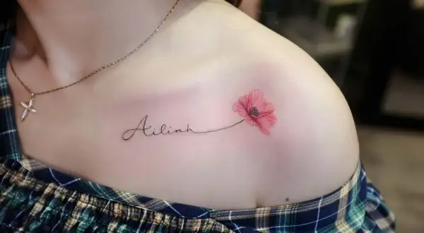 Ein zartes Tattoo mit dem Namen "Ailinh" und einer roten Mohnblume auf der Schulter.