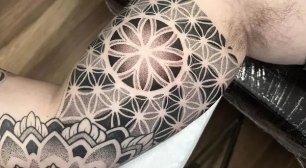 Ein Mann trägt ein geometrisches Tattoo am Oberarm. Das Muster erinnert an eine Blume des Lebens und ist fein gestochen.