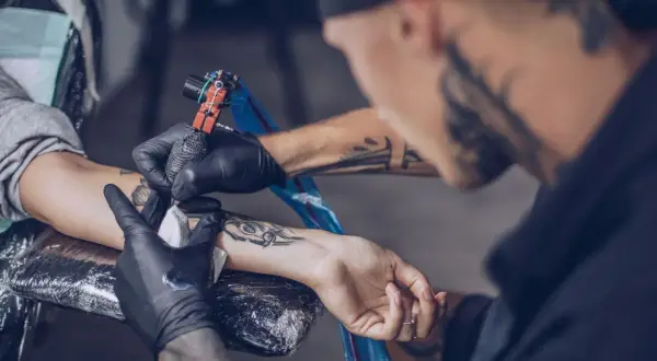 Ein Mann erhält ein intimtattoo am Arm. Der Tätowierer arbeitet sorgfältig mit der Maschine.