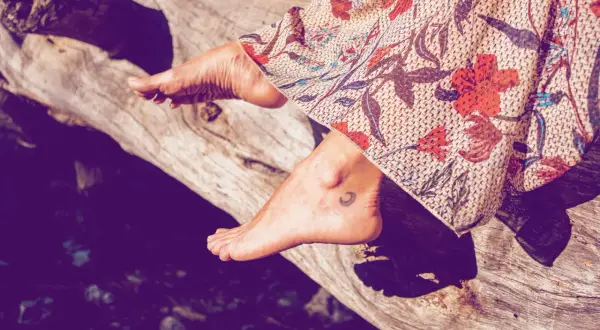 Ein Fuß mit einem kleinen Mond-Tattoo ruht auf einem Baumstamm, bedeckt von einem gemusterten Stoff.
