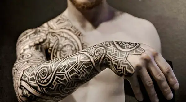 Mann mit beeindruckenden Sleeve Tattoo Ideen, die sich über Arm und Schulter erstrecken. Geometrische Muster und geschwungene Linien.