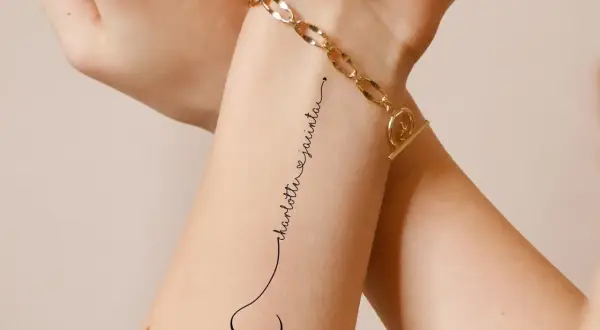 Ein dezentes Tattoo mit den Namen "Charlotte & Jacinta" in geschwungener Schrift, verbunden mit einem kleinen Herz.