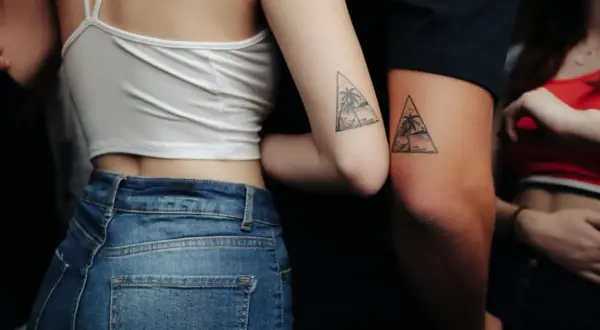 Zwei Arme mit passenden Dreiecks-Tattoos, die Palmen und eine Hängematte zeigen. Eine schöne Tattoo Idee Familie, die Verbundenheit symbolisiert.