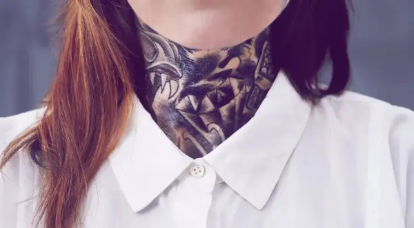 Ein detailreiches, old school Hals Tattoo mit einem Wolfskopf und scharfen Zähnen, bedeckt den Hals einer Person, die ein weißes Hemd trägt.