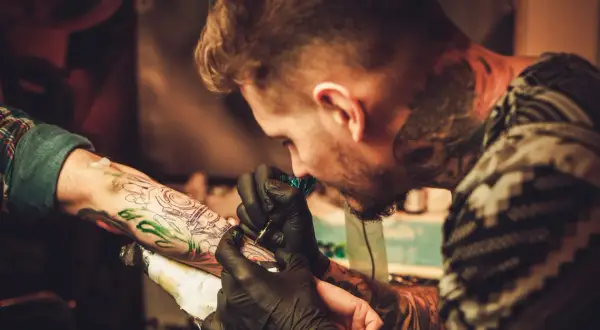 Ein Tätowierer mit vielen Rapper-Tattoos sticht einem Kunden ein neues Motiv auf den Arm.