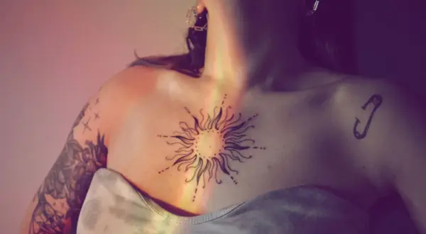 Ein Sonnen-Tattoo auf der Brust symbolisiert das beste Leben. Ein Sicherheitsnadel-Tattoo auf der Schulter.