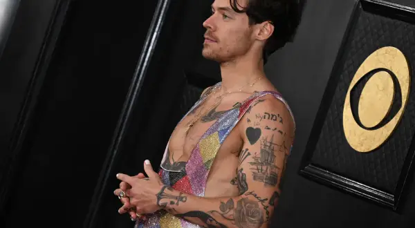Harry Styles mit vielen Tätowierungen, die als Inspiration für Tattoo Ideen Mann dienen. Ein Herz, ein Schiff und Rosen sind zu sehen.