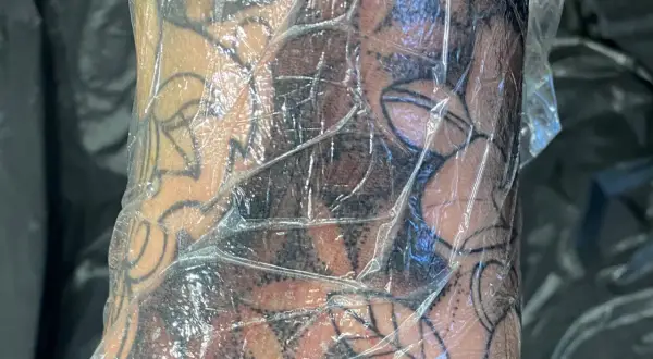 Frische Tattoo-Haut geht ab, bedeckt mit Folie. Das Motiv zeigt dunkle Schattierungen und klare Linien.