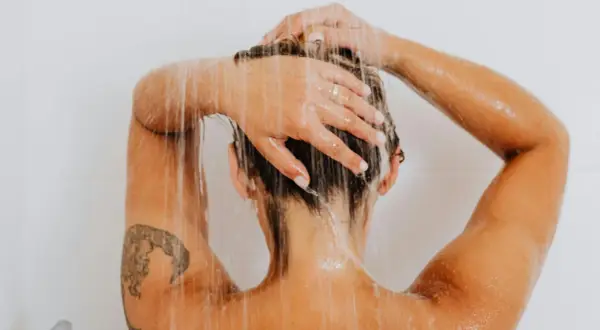 Frauenkopf unter der Dusche, Wasser rinnt über Schultern und Arme mit einem frischen Tattoo.