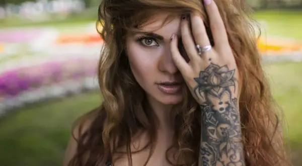 Frau mit welligem Haar und einem detaillierten Mandala Handgelenk Tattoo, das sich über ihren Unterarm erstreckt.