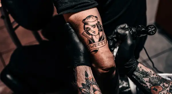 Ein Tätowierer vervollständigt ein "second skin tattoo" einer Frau mit dem Schriftzug "SWEETY" auf einem Arm.
