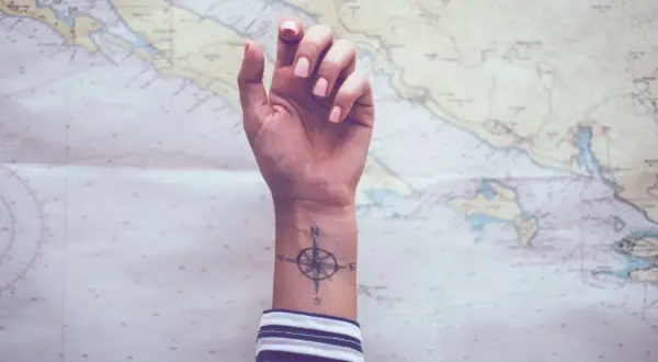 Ein Handgelenk mit einem Kompass-Tattoo, das die Verbundenheit von Geschwistern symbolisiert, vor einer Seekarte.
