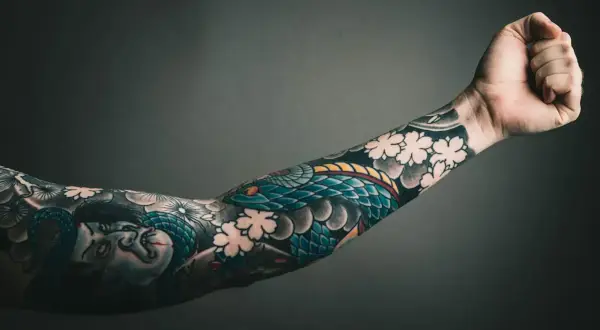 Ein Arm mit einem detailreichen Tattoo, das eine Schlange und Kirschblüten zeigt. Die Botschaft "alles wird gut" ist in diesem Kunstwerk auf der Haut verewigt.