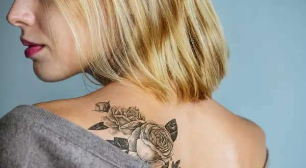 Blonde Frau mit einem Rosen-Tattoo ohne Folie auf der Schulter.