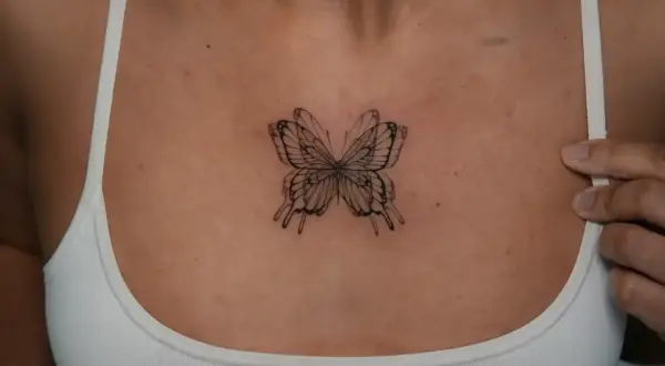 Zartes Fineline-Tattoo eines Schmetterlings zwischen den Brüsten, das wie ein filigranes Kunstwerk wirkt.