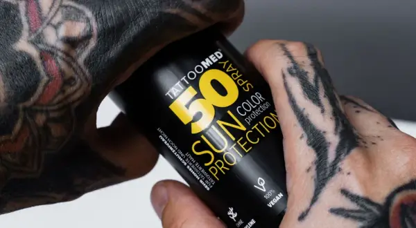 Hände mit Tattoos halten eine Sonnencreme-Spraydose. Die Dose schützt die Haut und das Tattoo vor der Sonne.