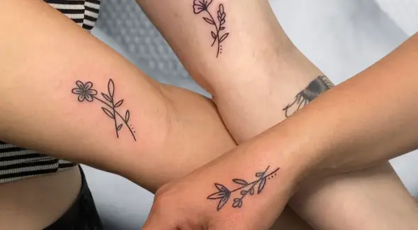 Drei Arme zeigen zarte, elegante Tattoos von Blumen und Zweigen.