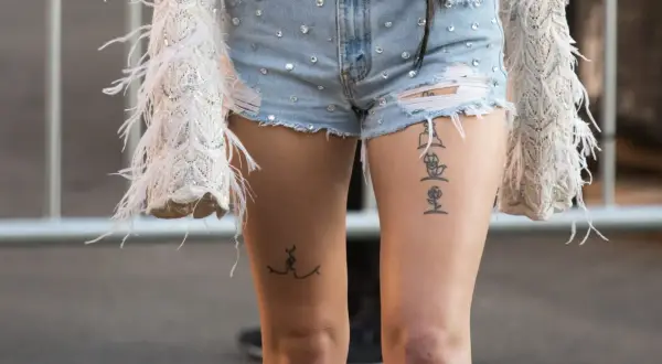 Ein Oberschenkel Tattoo Schriftzug mit einer Rose und einer stilisierten Figur.