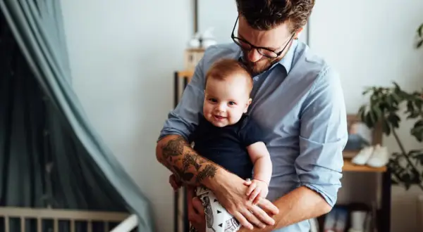 Ein Mann hält sein Baby. Auf seinem Unterarm sind Tätowierungen, die an die Namen seiner Kinder erinnern.