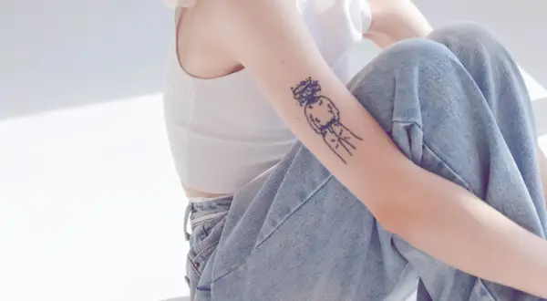 Ein Arm mit einem abstrakten Tattoo, das eine Figur mit einem Kranz darstellt. Die Linien sind klar und dick, ein typisches Merkmal für ein tattoo dicke linien.