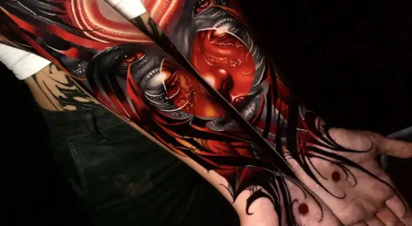 Arm-Tattoos mit roten Tattoos, die ein dämonisches Gesicht mit roten Augen und scharfen Zähnen darstellen.