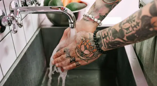 Hände mit Tattoos werden unter fließendem Wasser gewaschen, um die Pflege nach dem Duschen nach dem Tattoo zu gewährleisten.