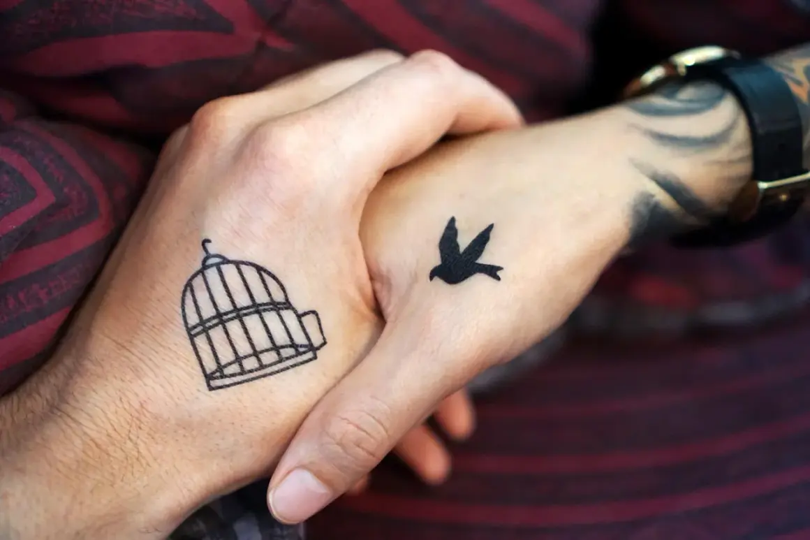 Zwei Hände mit leichten Tattoos zum selber zeichnen: Ein Vogel fliegt aus einem Käfig.