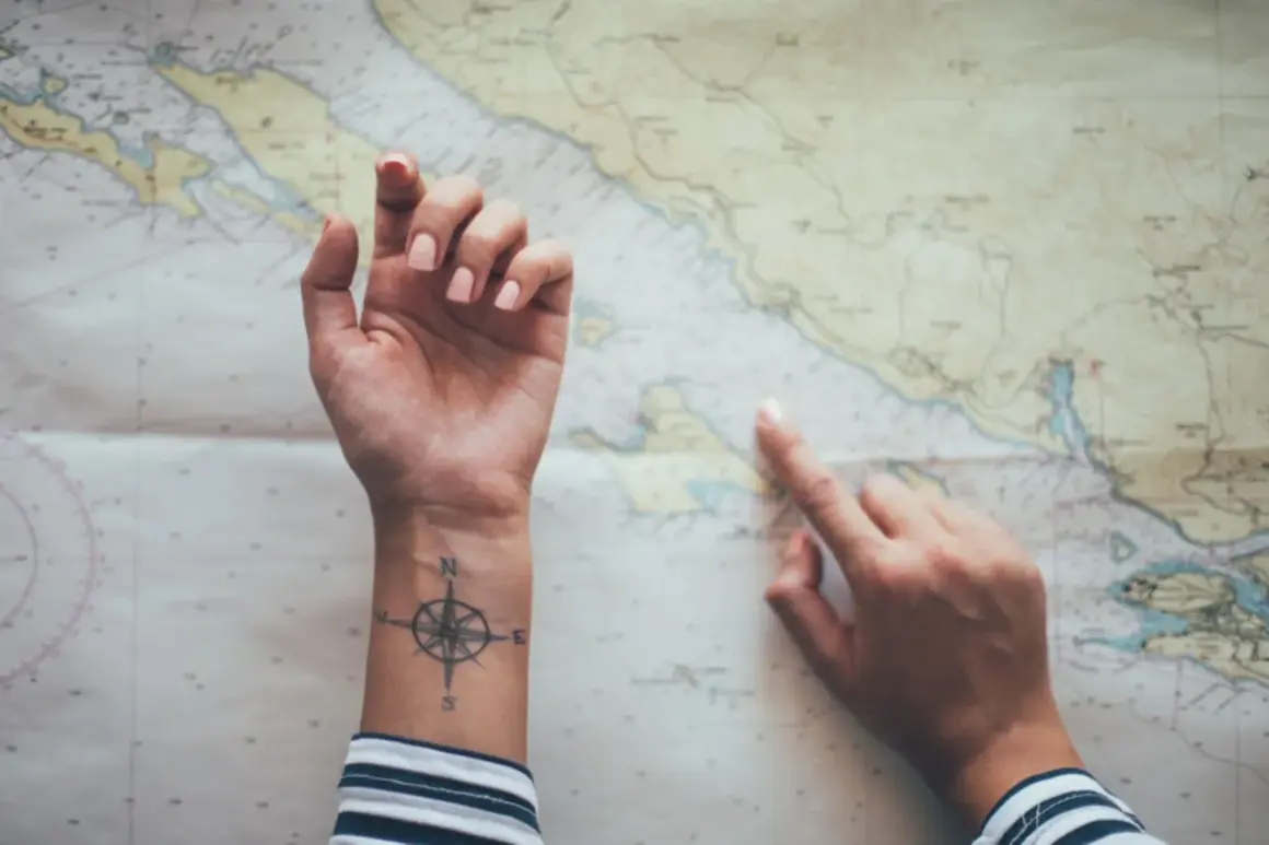 Hände über einer Seekarte, eine mit einem Kompass-Tattoo, das an ein Partner Tattoo Koordinaten erinnert.