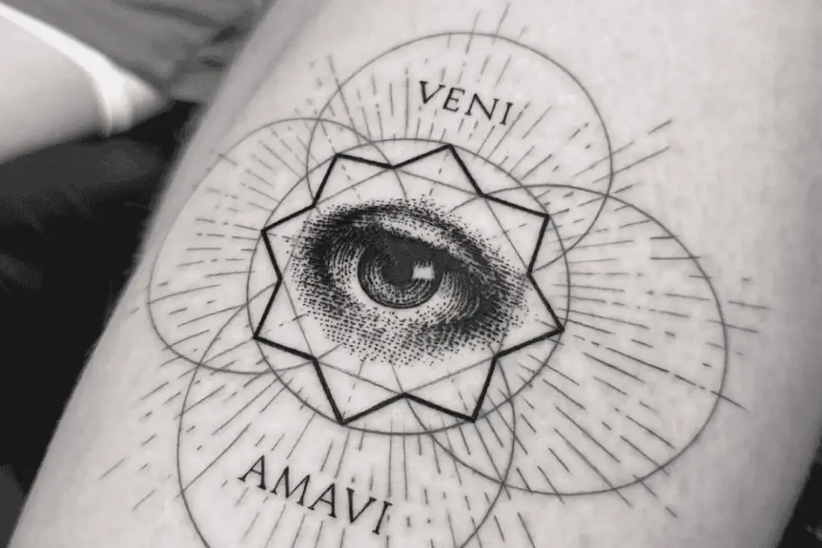 Ein filigranes Fineline Tattoo am Oberarm einer Frau zeigt ein Auge inmitten geometrischer Formen und der Worte "VENI AMAVI".