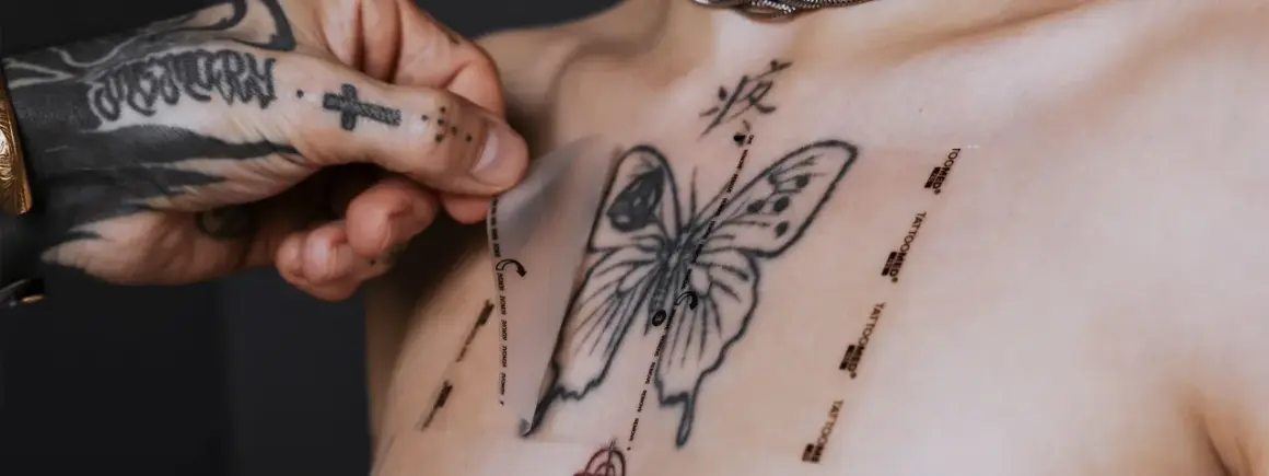 Frische tattoo pflege: Frischhaltefolie wird vorsichtig auf ein frisch gestochenes Schmetterlingstattoo auf der Brust aufgelegt.