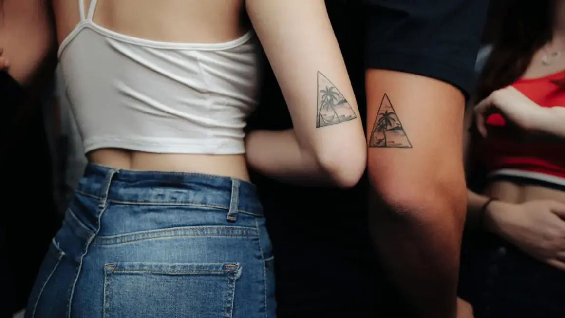 Zwei Arme mit passenden Dreiecks-Tattoos, die Palmen und eine Hängematte zeigen. Eine schöne Tattoo Idee Familie, die Verbundenheit symbolisiert.