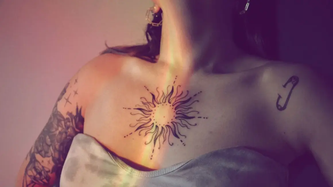 Ein Sonnen-Tattoo auf der Brust symbolisiert das beste Leben. Ein Sicherheitsnadel-Tattoo auf der Schulter.