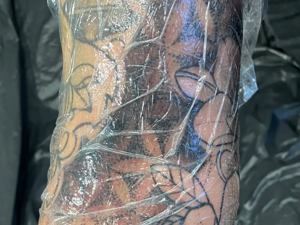 Frische Tattoo-Haut geht ab, bedeckt mit Folie. Das Motiv zeigt dunkle Schattierungen und klare Linien.
