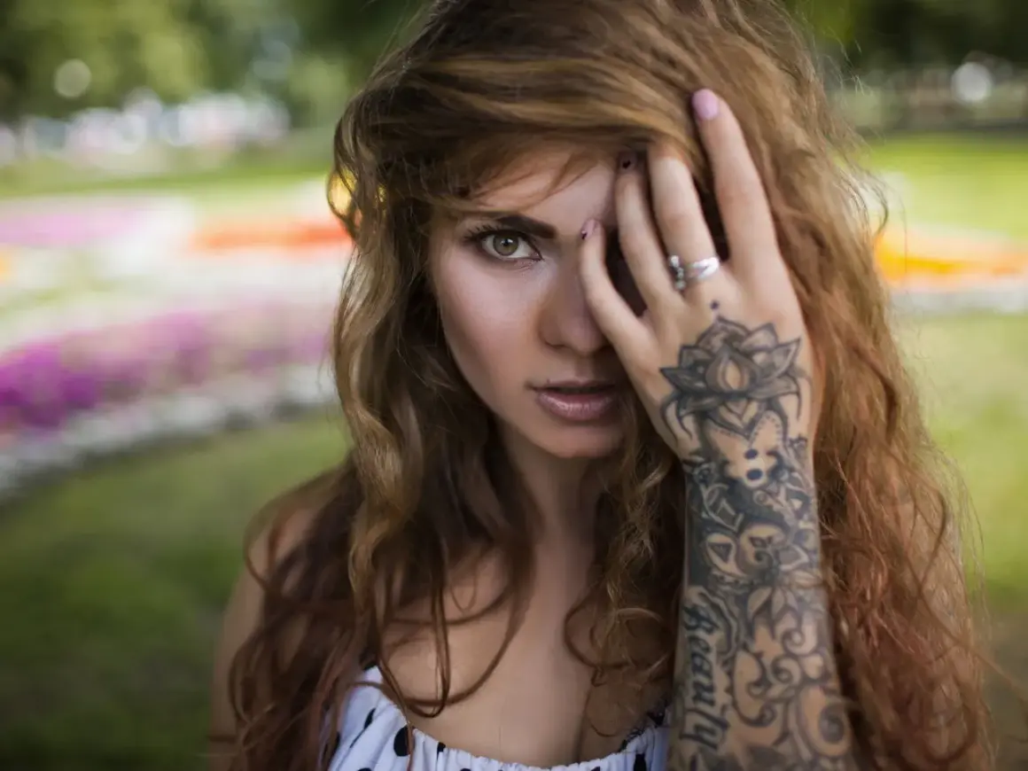 Frau mit welligem Haar und einem detaillierten Mandala Handgelenk Tattoo, das sich über ihren Unterarm erstreckt.