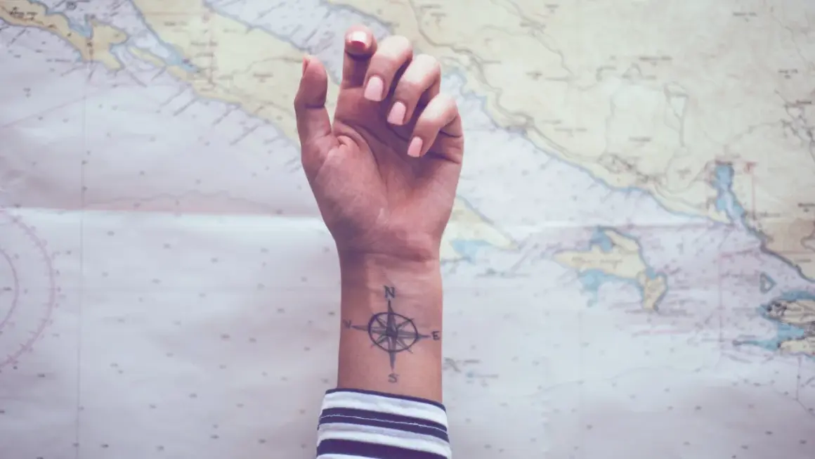 Ein Handgelenk mit einem Kompass-Tattoo, das die Verbundenheit von Geschwistern symbolisiert, vor einer Seekarte.
