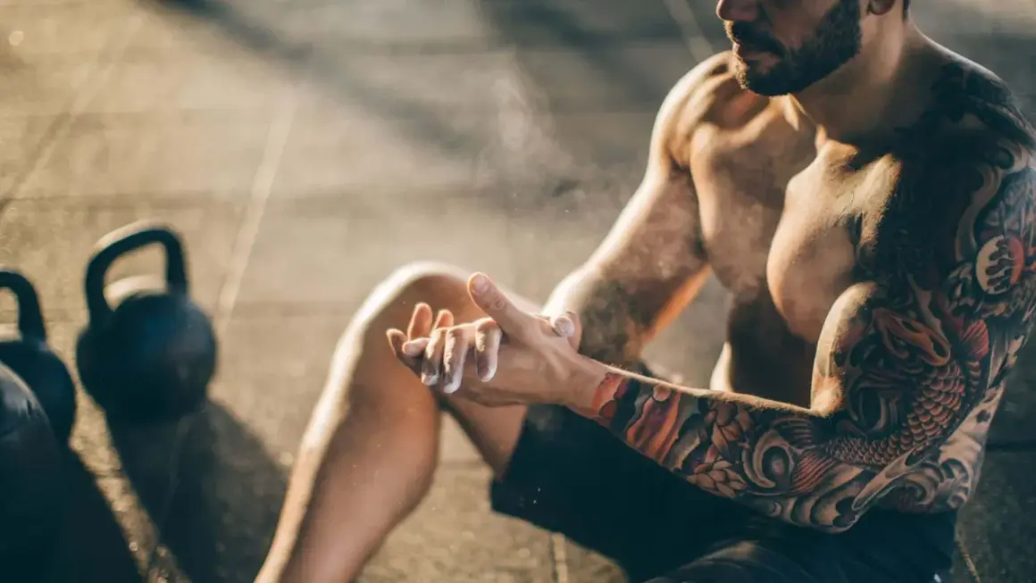 Ein Mann mit beeindruckenden herren tattoos bereitet sich mit Magnesium vor. Kettlebells liegen im Hintergrund.