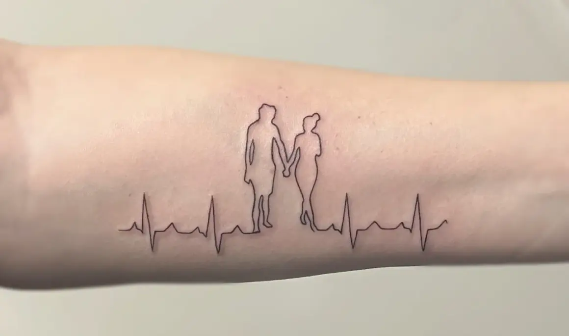 Ein Fineline Tattoo zeigt ein Paar, das Händchen hält, über einer EKG-Linie. Ein schönes Vorher-Nachher-Beispiel für zarte Linienkunst.