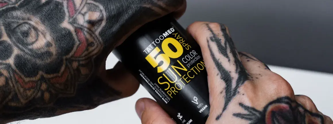 Hände mit Tattoos halten eine Sonnencreme-Spraydose. Die Dose schützt die Haut und das Tattoo vor der Sonne.