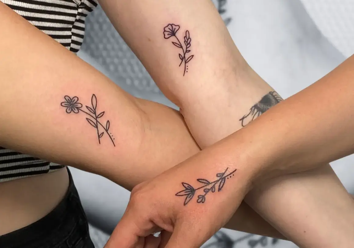 Drei Arme zeigen zarte, elegante Tattoos von Blumen und Zweigen.