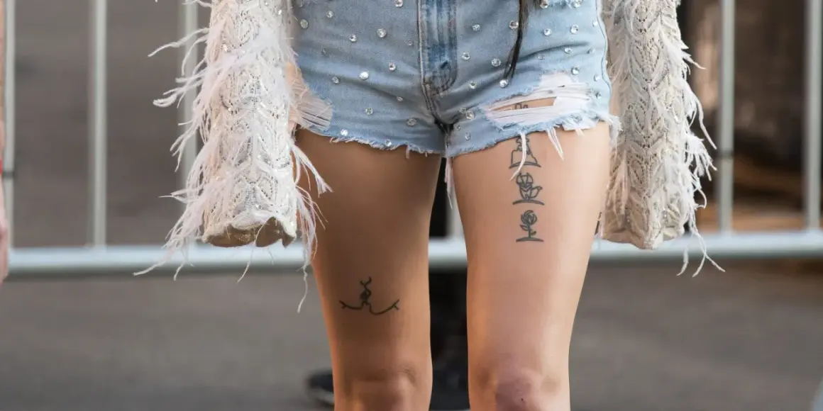 Ein Oberschenkel Tattoo Schriftzug mit einer Rose und einer stilisierten Figur.