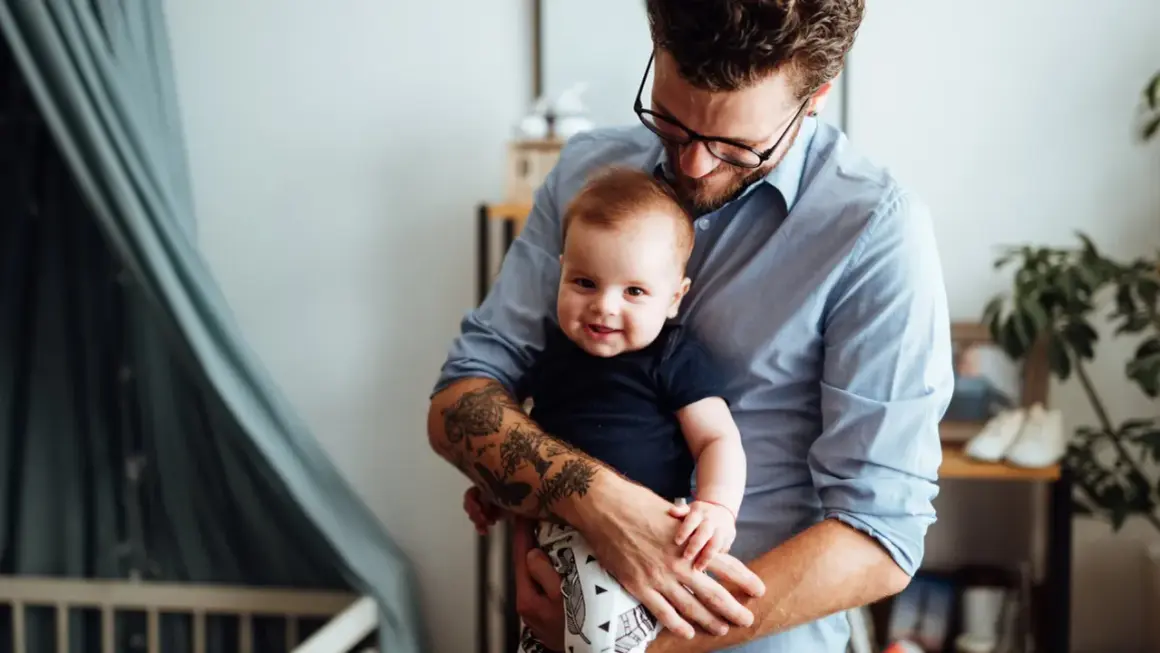 Ein Mann hält sein Baby. Auf seinem Unterarm sind Tätowierungen, die an die Namen seiner Kinder erinnern.