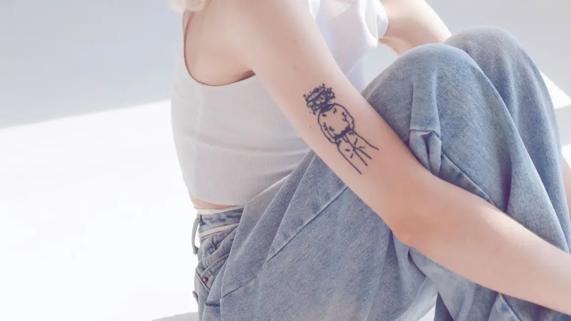 Ein Arm mit einem abstrakten Tattoo, das eine Figur mit einem Kranz darstellt. Die Linien sind klar und dick, ein typisches Merkmal für ein tattoo dicke linien.