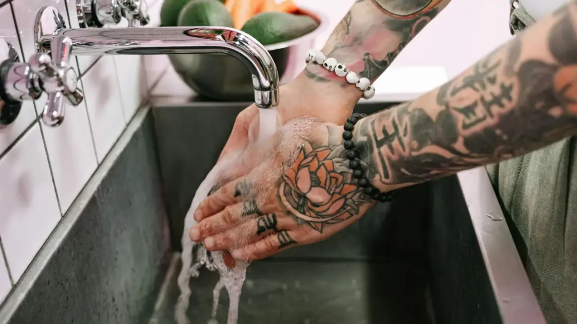 Hände mit Tattoos werden unter fließendem Wasser gewaschen, um die Pflege nach dem Duschen nach dem Tattoo zu gewährleisten.