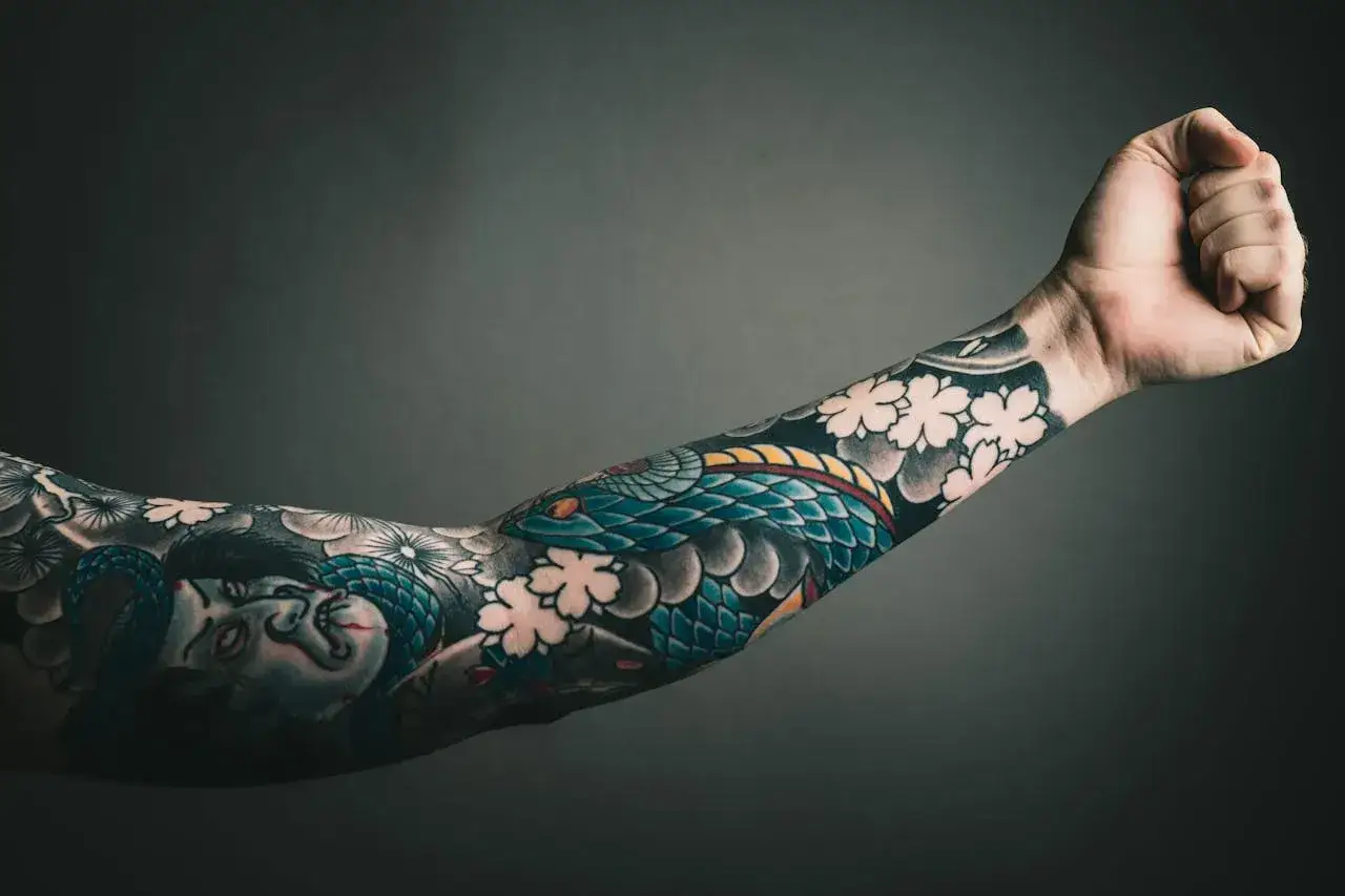 Ein Arm voller Tätowierungen: eine Schlange, Kirschblüten und ein Gesicht. Die sleeve tattoo kosten sind hoch, aber die Kunst ist es wert.