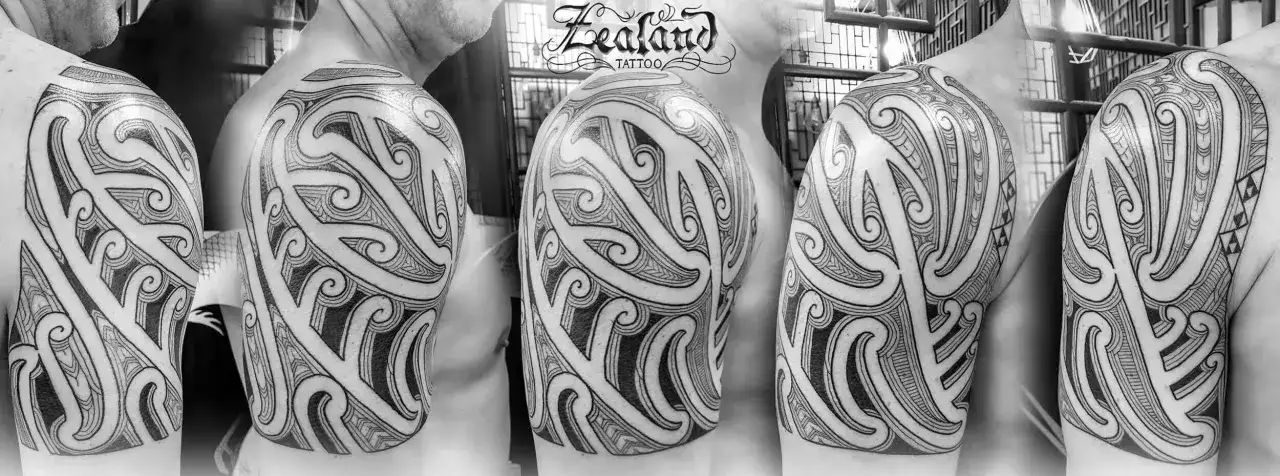 Ein Mann trägt ein detailreiches Maori-Tattoo auf seiner Schulter und seinem Oberarm. Die Linien sind klar und die Muster sind komplex.