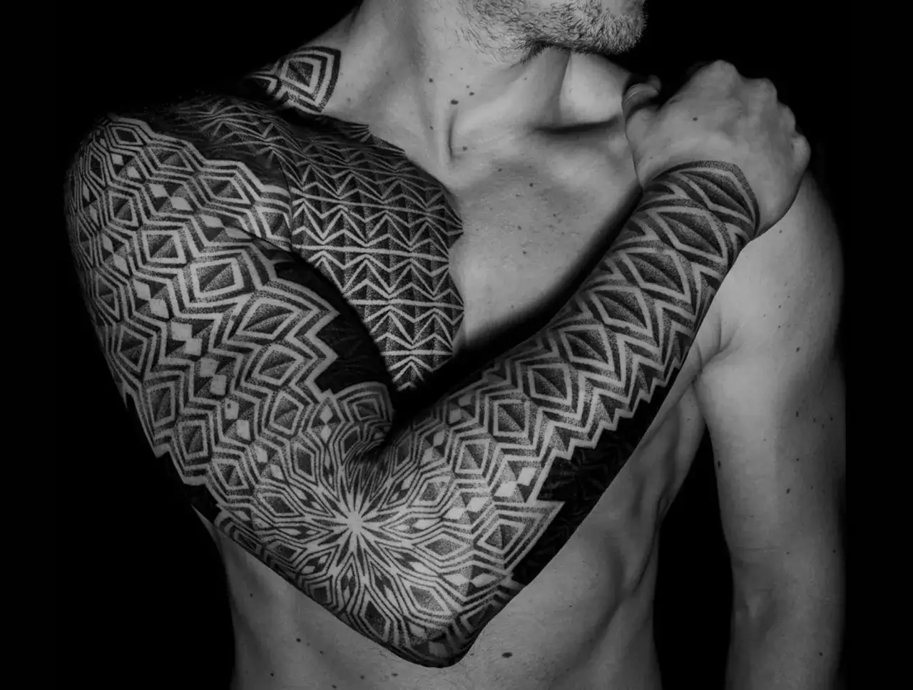 Mann mit geometrischen Tattoo-Punkten, die sich über Arm und Schulter erstrecken. Ein faszinierendes Muster aus Linien und Punkten.