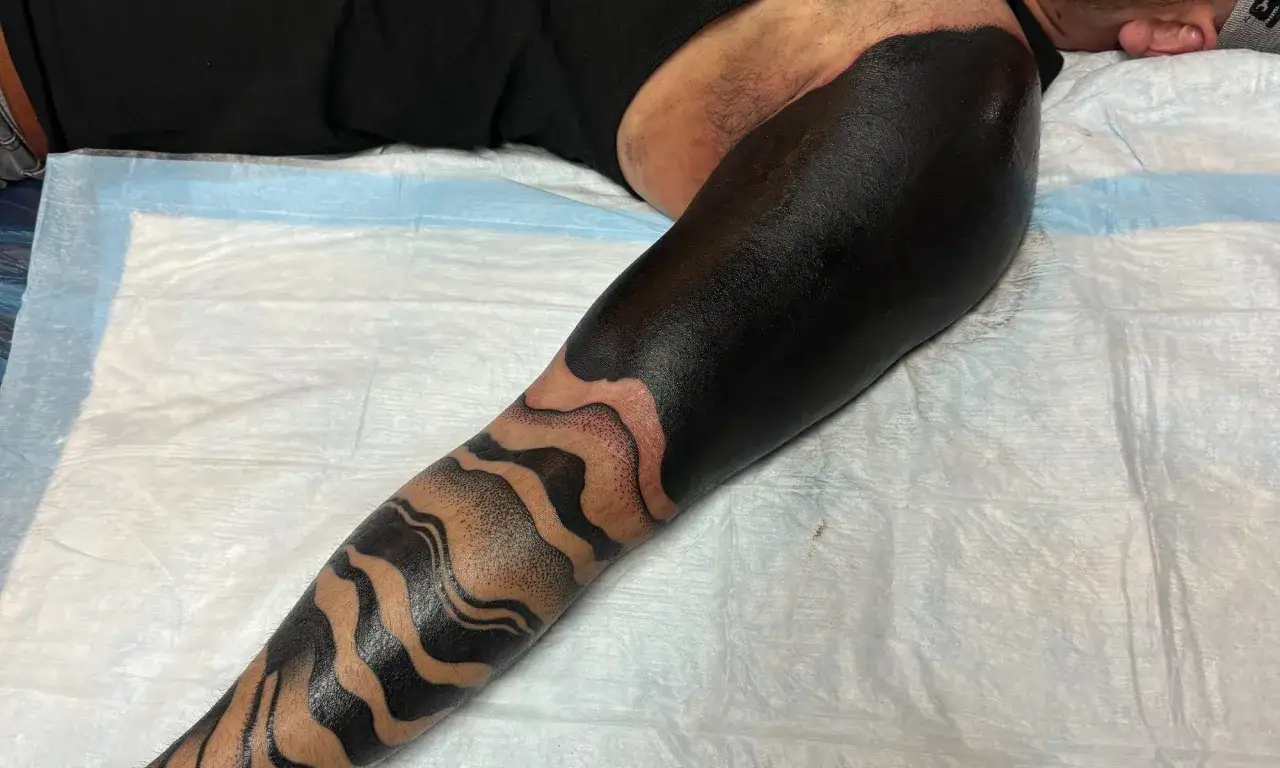 Ein Unterarm mit einem auffälligen all black tattoo, das in Wellenmuster übergeht.