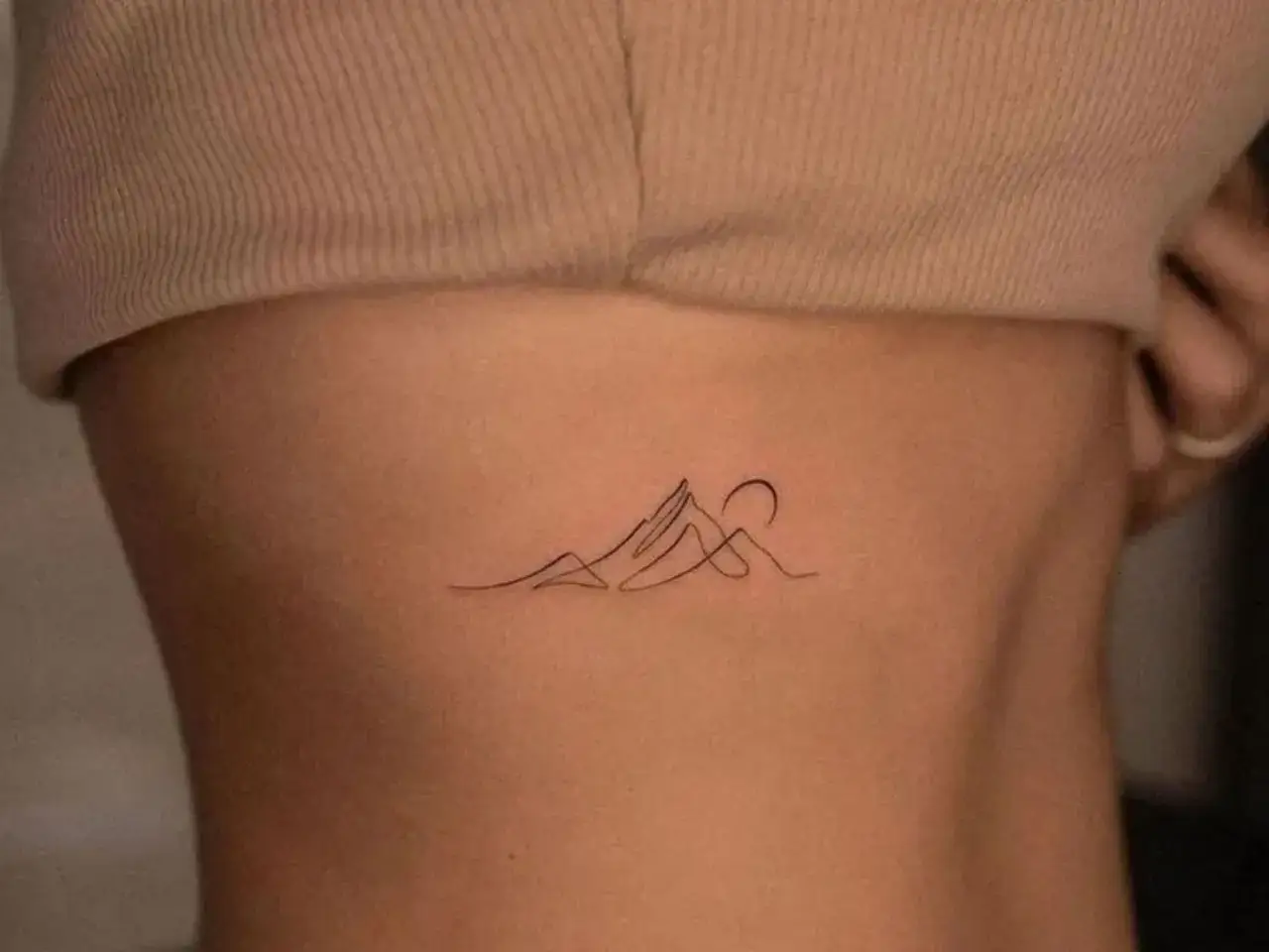 Ein zartes Fineline Tattoo mit Bergen und einer aufgehenden Sonne auf der Haut.