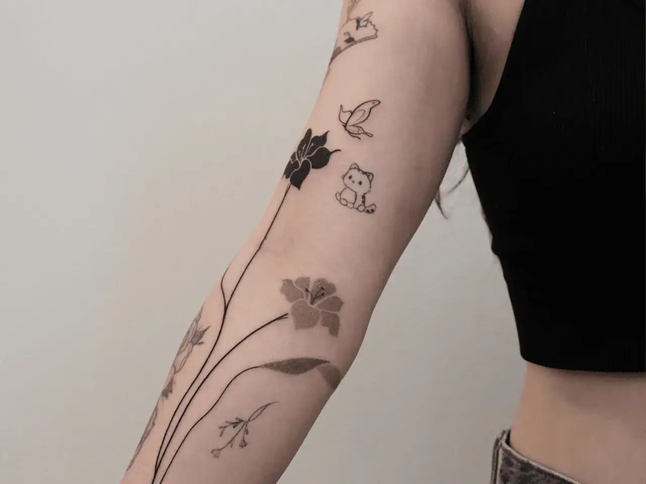 Ein zarter Armschmuck: filigrane Blumen, ein Schmetterling und ein süßes Kätzchen – was ist ein Fineline Tattoo? Zarte Linienkunst.