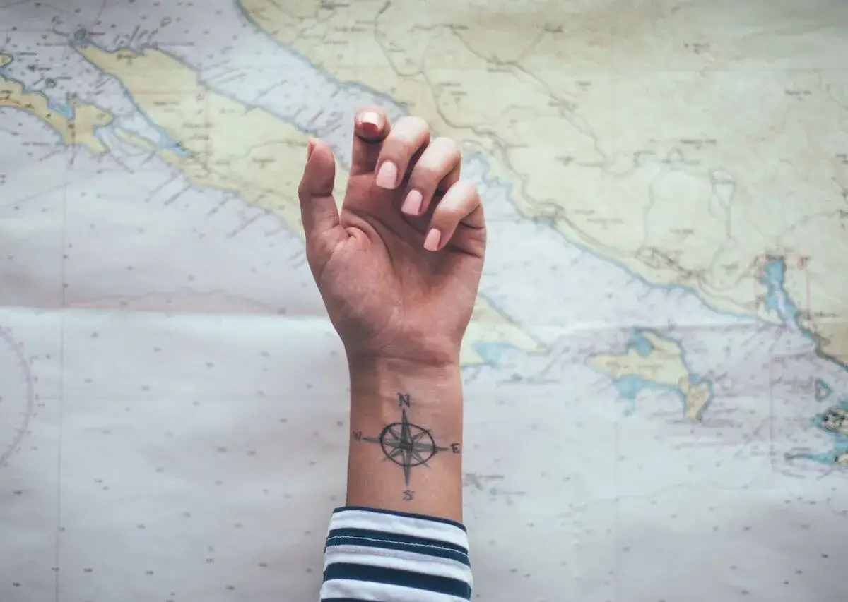 Ein Kompass-Tattoo am Handgelenk, ein Symbol f&uuml;r Reisen, vor einer Seekarte.